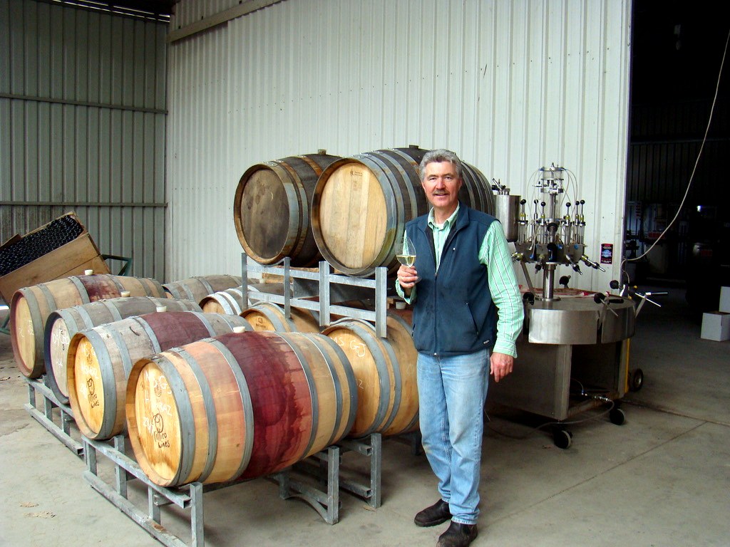 Mal Stewart standing beside wine barrels and cellar equipment.